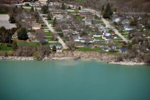 Aerial photo of water and buildings near the water. One house is balanced on the edge of a tall bluff over the water. 