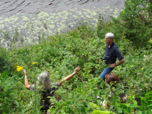 Man and woman standing near water and in tall grass. 