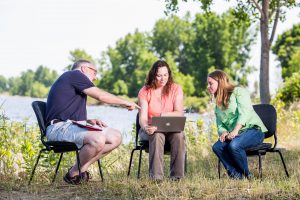 Man and two women sitting outside looking at a laptop computer 