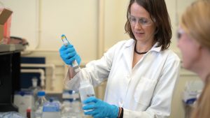 Woman wearing lab goggles, gloves and a lab coat in a lab. 