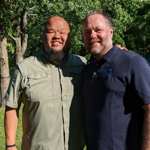 Two men standing side-by-side outdoors. 