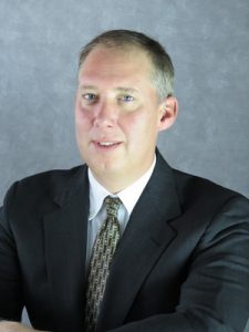 Close-up of a smiling person wearing a suit and tie. 