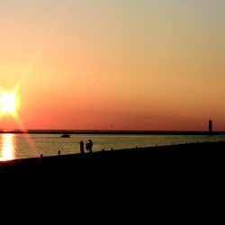 Sunrise over water and silhouettes of people on the shore
