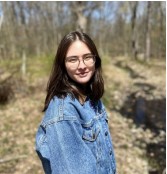 Smiling person standing in a grassy, wooded area. 