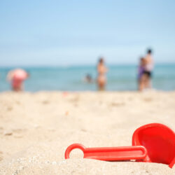 A red children's toy buried in beach sand