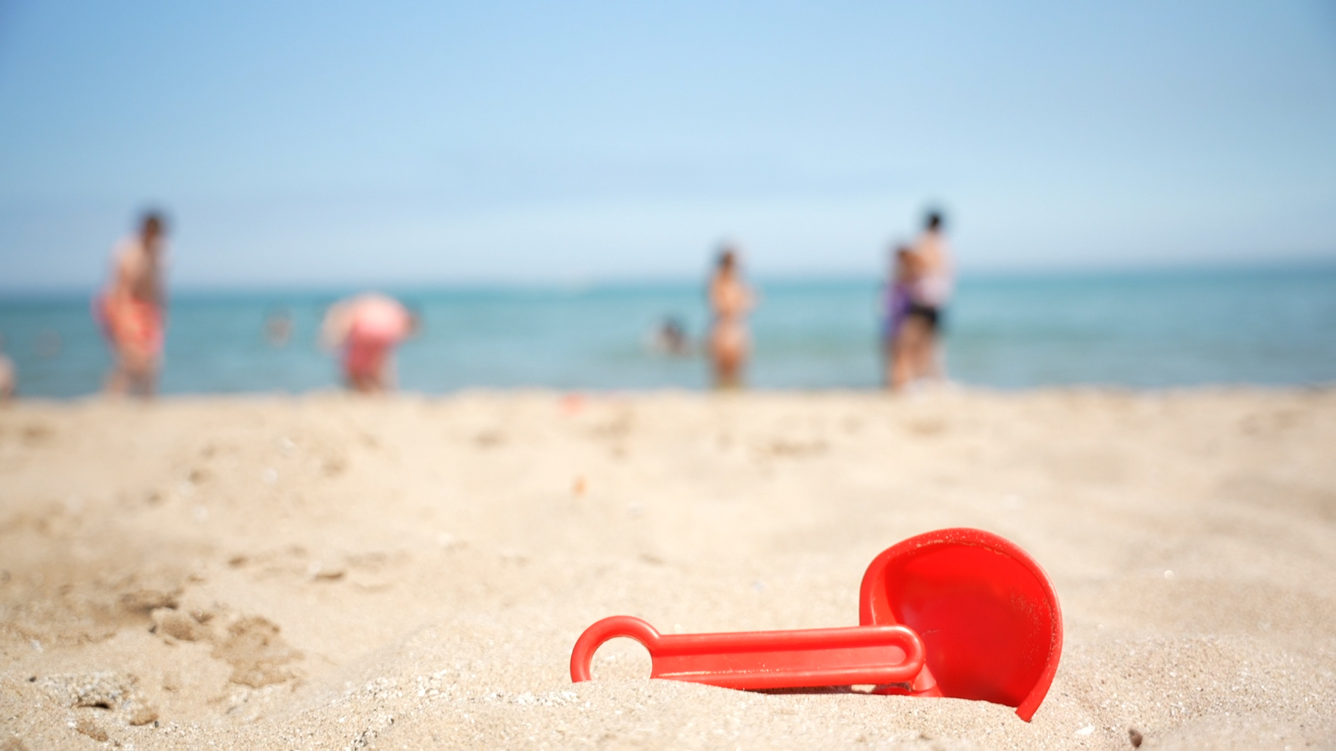 A red children's toy buried in beach sand