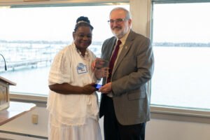 Two people stand side by side and both holding an award 