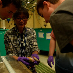 Deng holds up two yellow perch as two lab students look on.