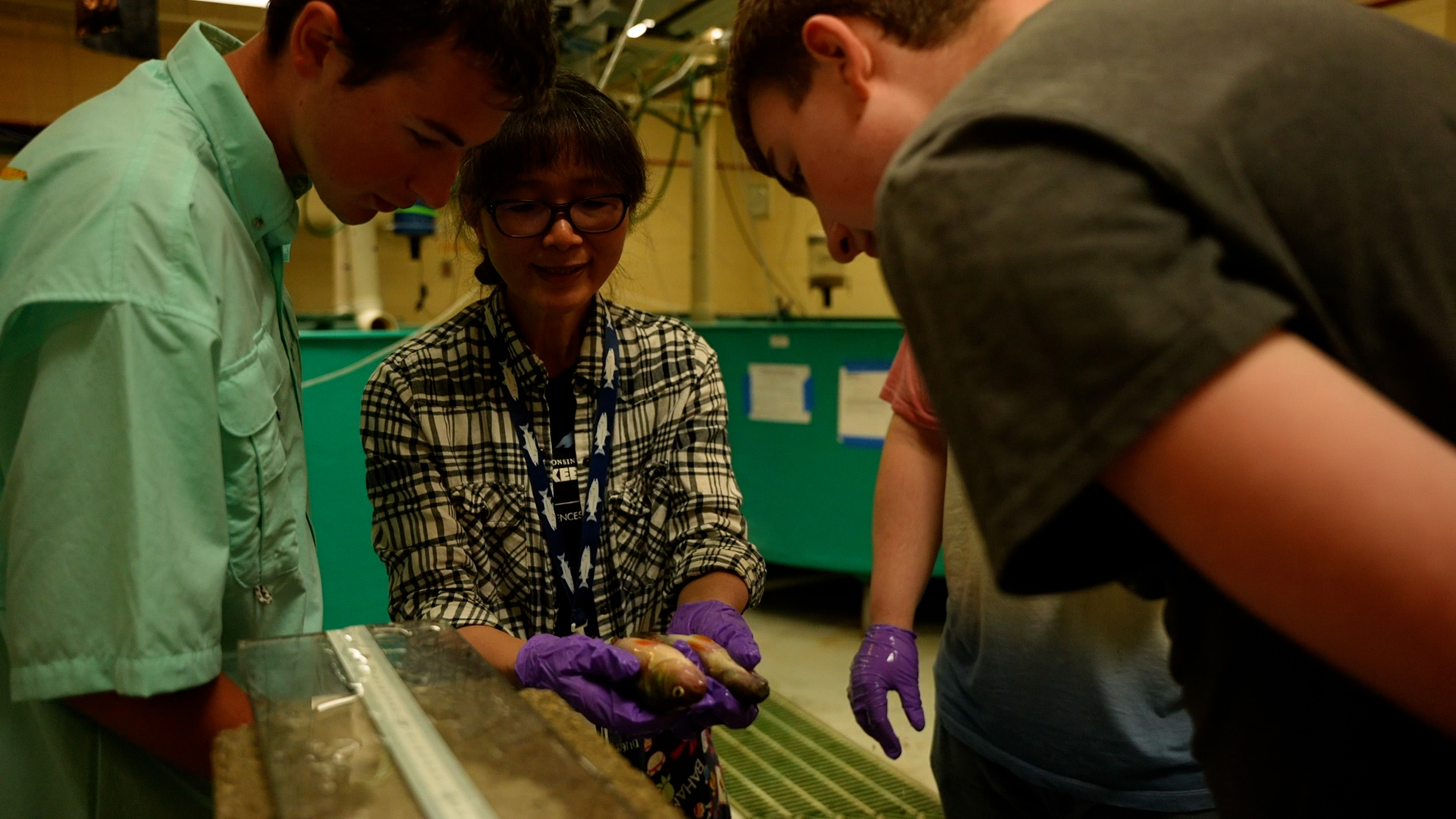 Deng holds up two yellow perch as two lab students look on.