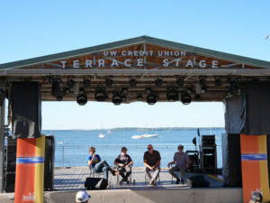 Four people sitting on a stage with a lake behind them. 