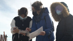 Group of three people standing outside in the wind and looking at a piece of paper. 