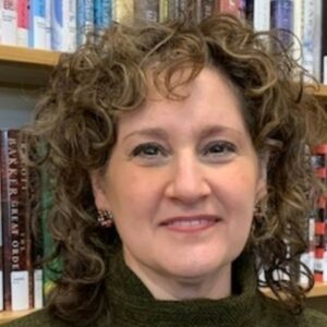 Close-up of smiling person standing in front of book shelves. 