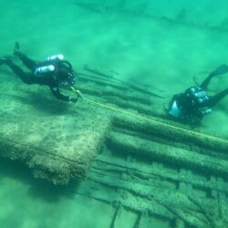 Two archeologists in scuba gear measure a shipwreck underwater