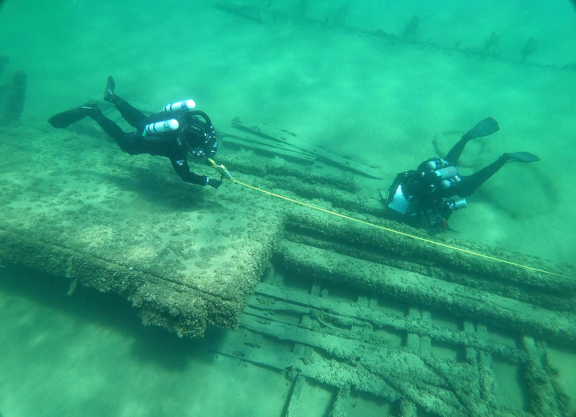 Two archeologists in scuba gear measure a shipwreck underwater