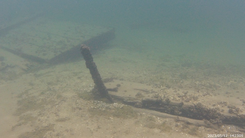 A piece of a shipwreck points upward from the lake sediment under which it is buried.
