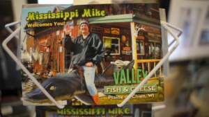 postcard showing Mike Valley sitting on a fiberglass musky