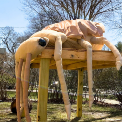 A giant, stuffed brown beetle sits on a wooden table outside