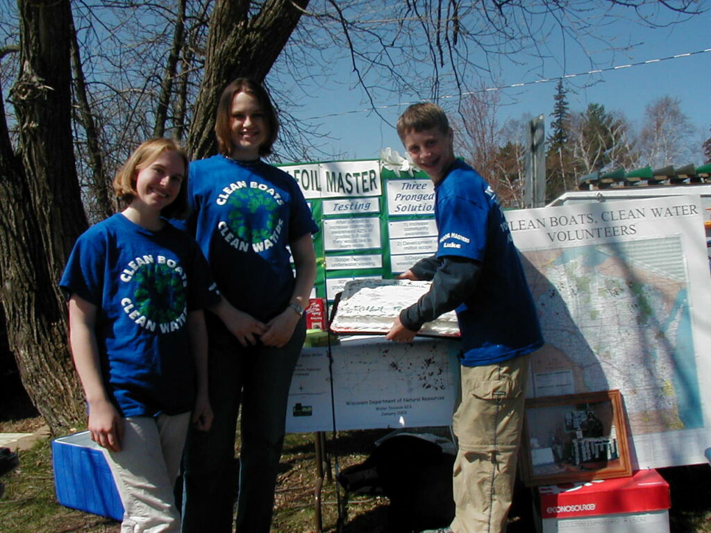 Students Maree, Janelle, and Luke, in the original Clean Boats, Clean Waters shirts, pose at their educational booth.