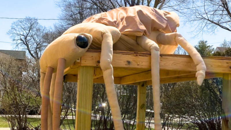 A giant, stuffed brown beetle sits on a wooden table outside.