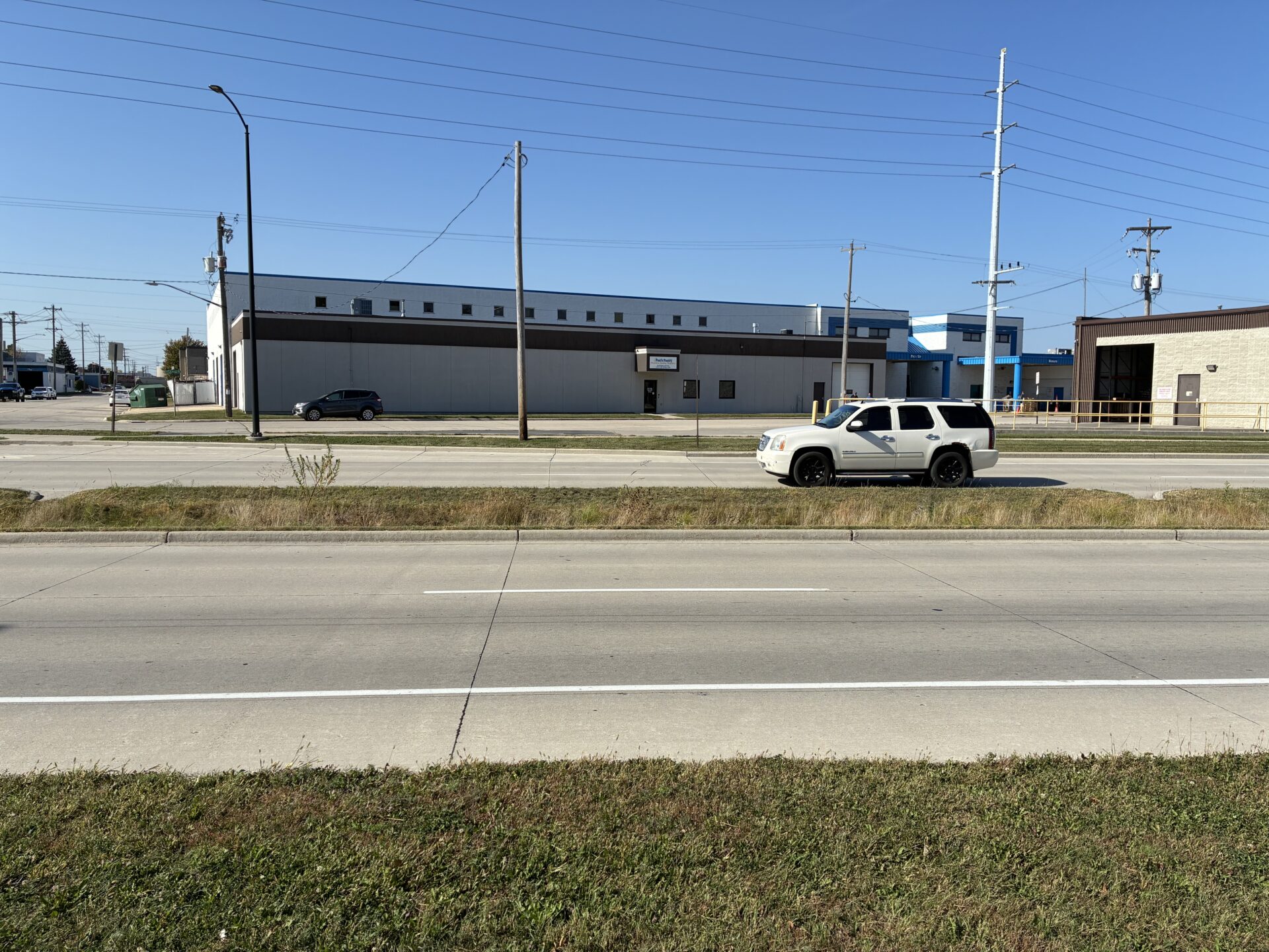 A white car drives past a grassy median