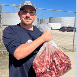 A man in a blue shirt and white hat holds up a big bag of red fish guts