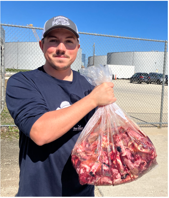 A man in a blue shirt and white hat holds up a big bag of red fish guts