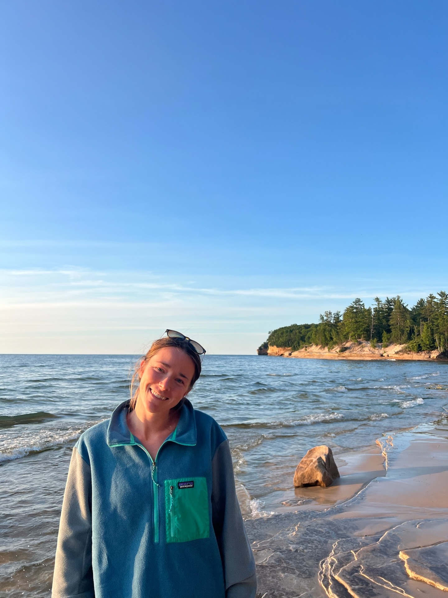 Cailin Young wears a blue jacket and stands on a Lake Superior beach