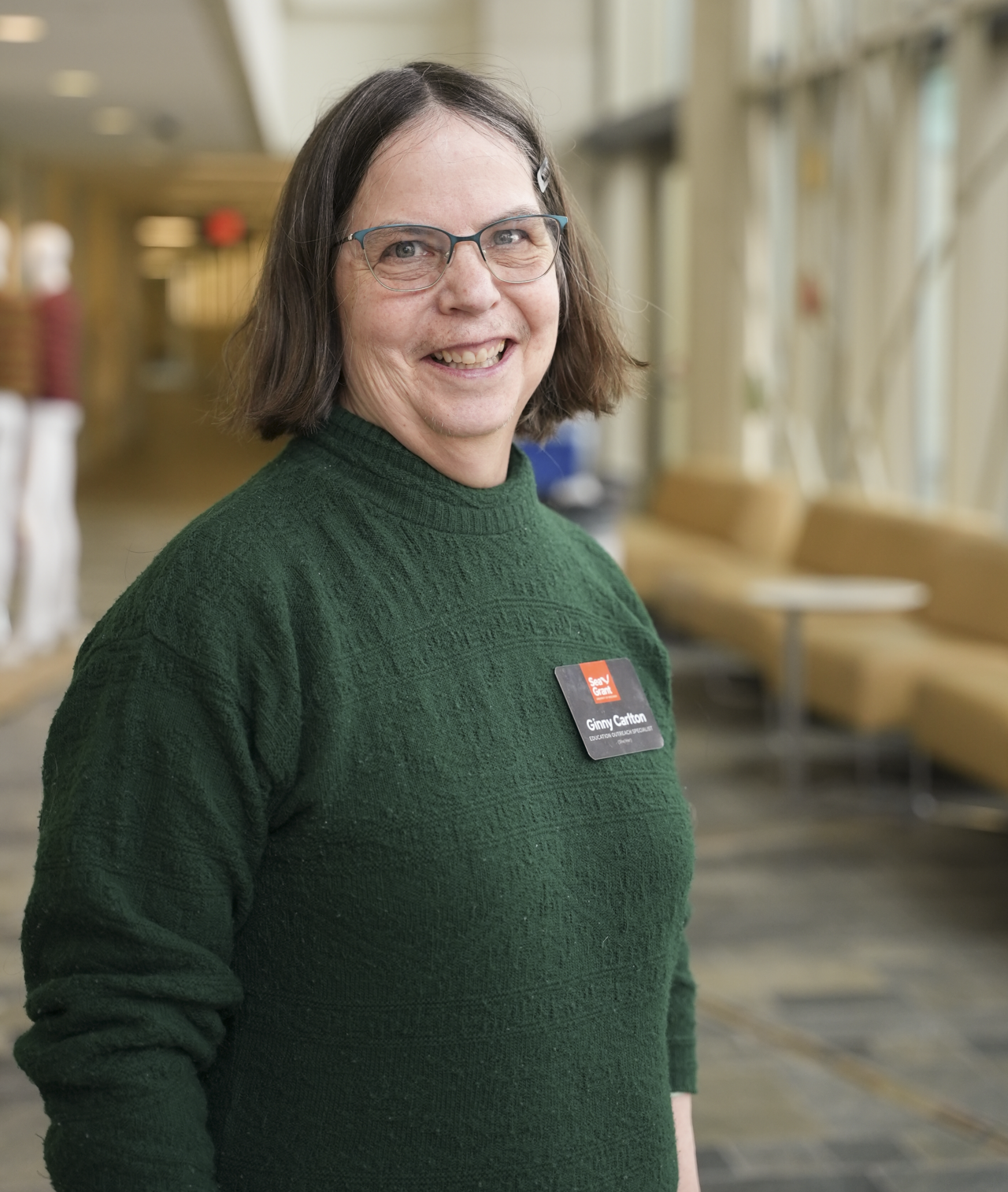 A woman with short dark hair, glasses, and a green sweater wearing a Sea Grant nametag