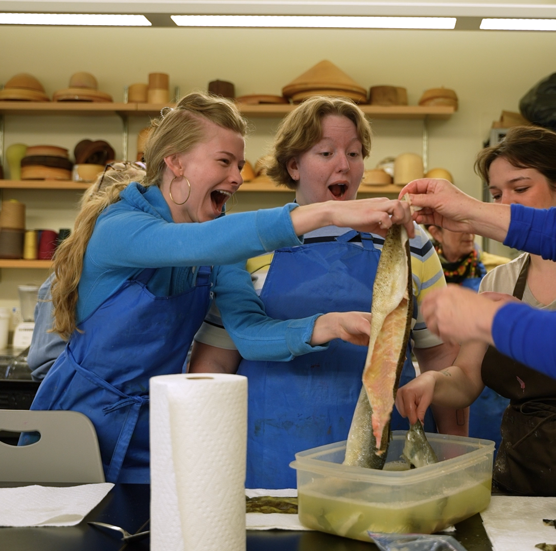 Two students look in excitedly at a fish skin they took from a bin full of water.